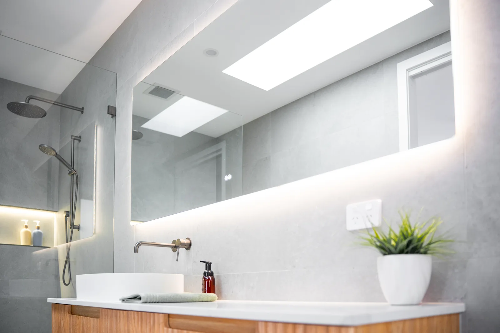 Backlit bathroom mirror with feature lighting above a timber vanity