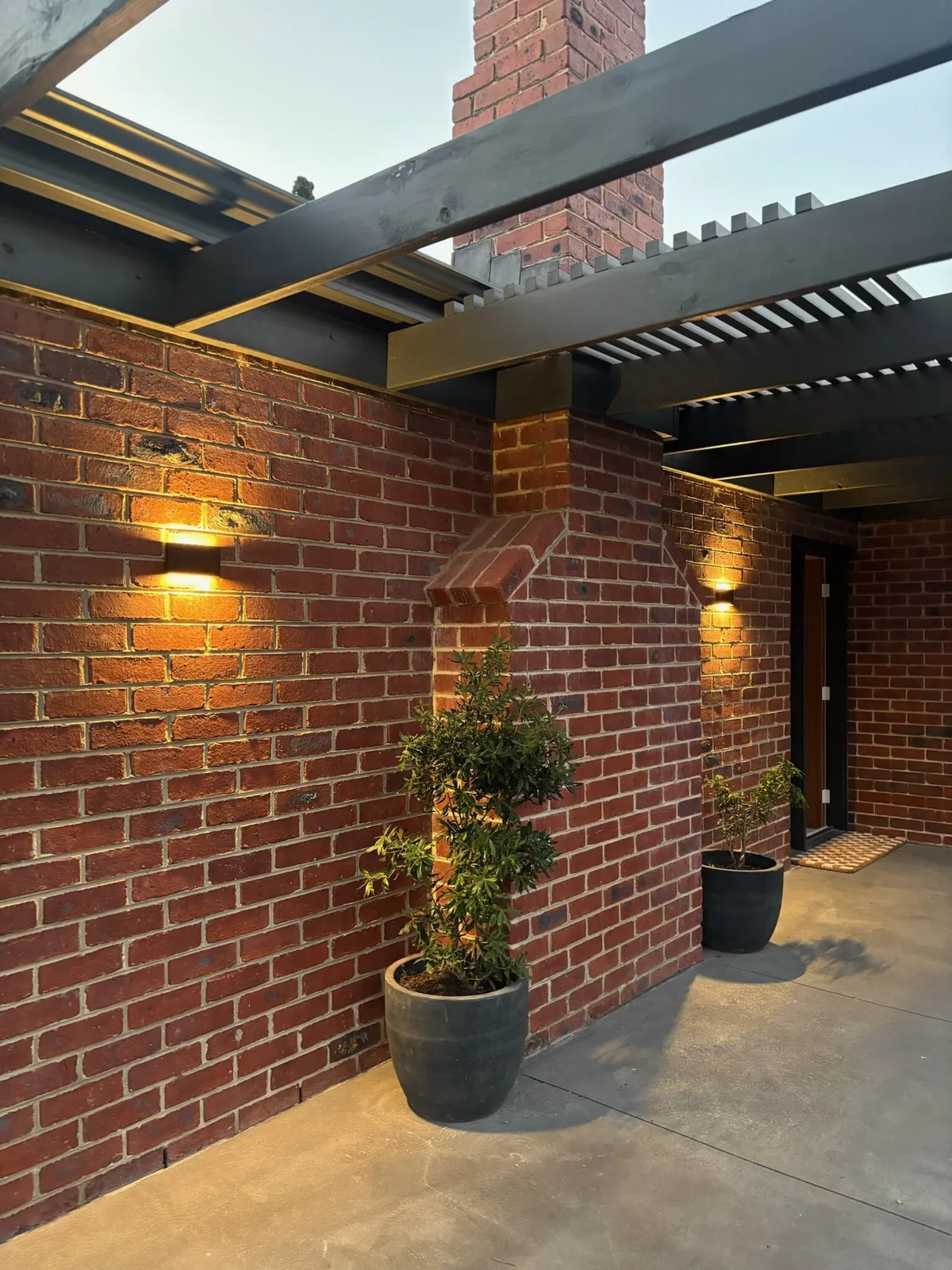 Outdoor wall lights glowing on a brick entryway at dusk